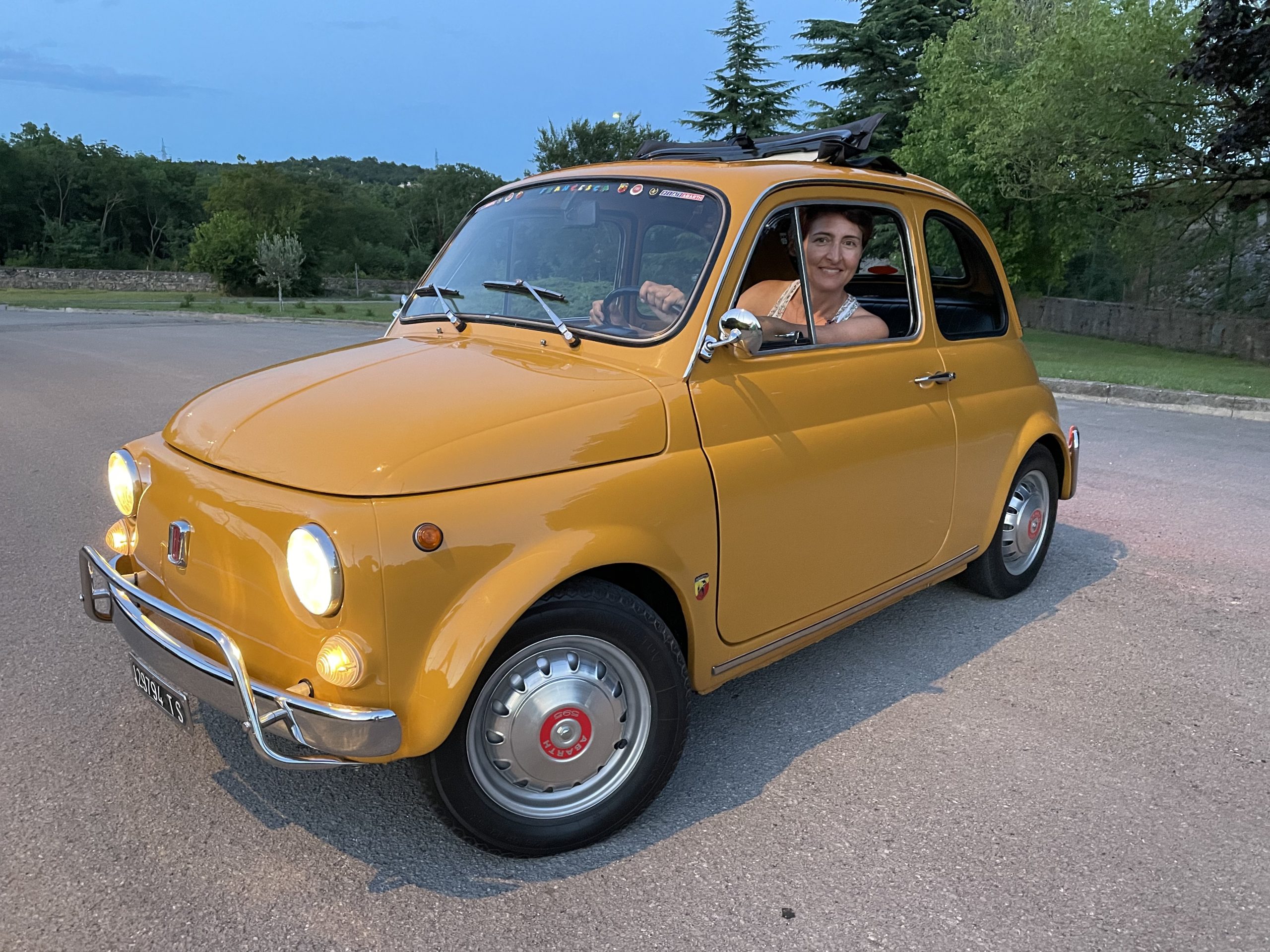 Francesca smiling from the driver's seat of a yellow vintage Fiat 500